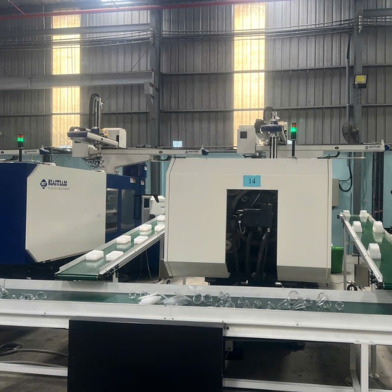 Cánh tay robot gắp hàng từ máy ép phun đặt lên băng tải